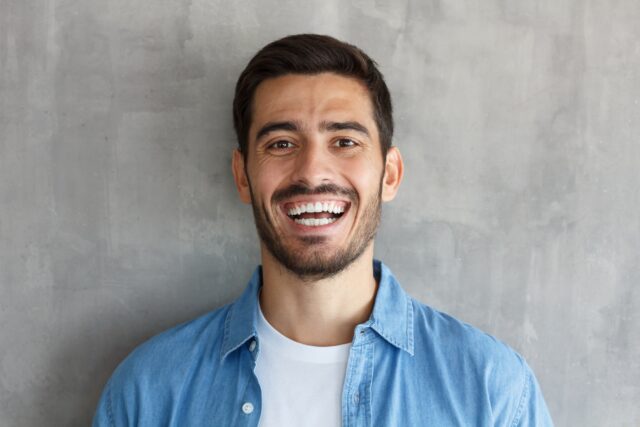 Young man smiles broadly, shows white perfect teeth