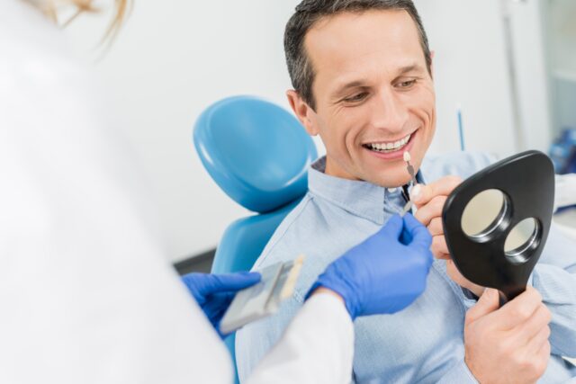 Male patient choosing tooth implant looking at mirror in modern dental clinic
